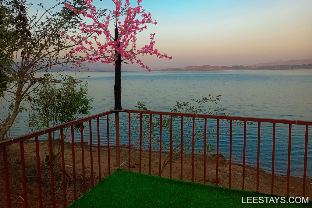 Scenic view at Diamond Resort near Pawna Lake, featuring a pink flowering tree and serene waters at dusk.