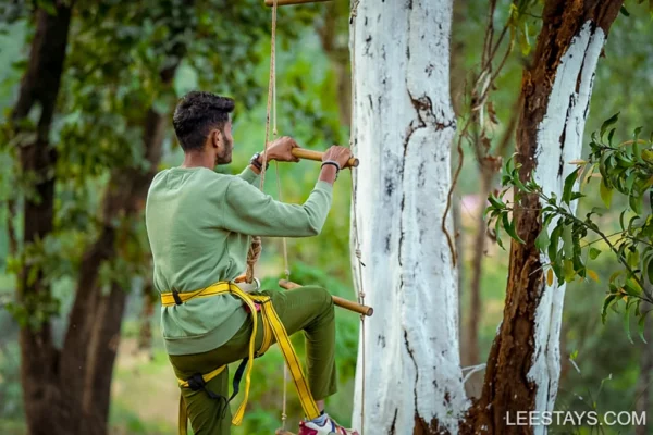 A person climbing a tree using a rope ladder at Diamond Resort near Pawna Lake, surrounded by lush greenery.