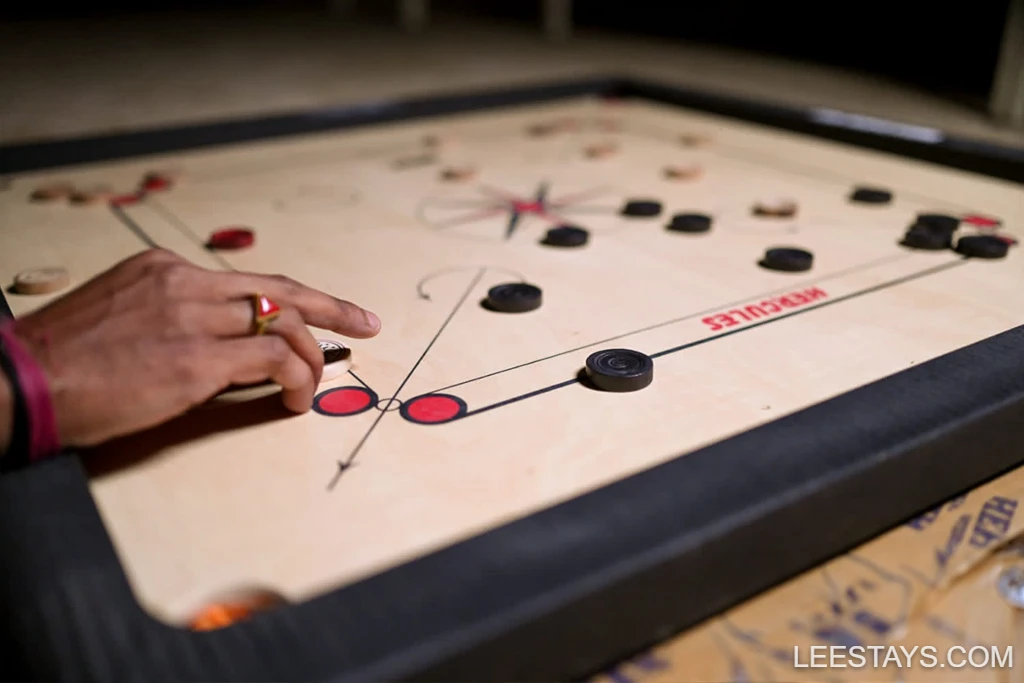 A hand poised over a carrom board in Diamond Resort by Pawna Lake, with game pieces positioned for play.