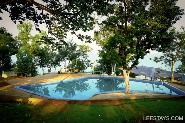 Tranquil view of the diamond resort pool surrounded by lush greenery near Pawna Lake, offering a serene atmosphere for relaxation.