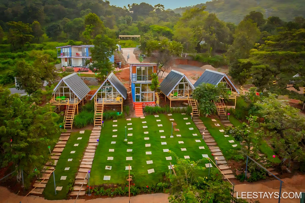Aerial view of Diamond Resort near Pawna Lake featuring unique triangular lodges, green lawns, and scenic landscaping.