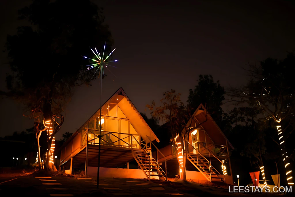 Two beautifully lit resort cottages at night, surrounded by trees, near Pawna Lake, showcasing a tranquil getaway atmosphere.