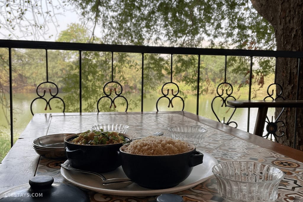 A scenic dining setup at a resort in Kamshet, featuring bowls of rice and vegetables with a serene lake view in the background.