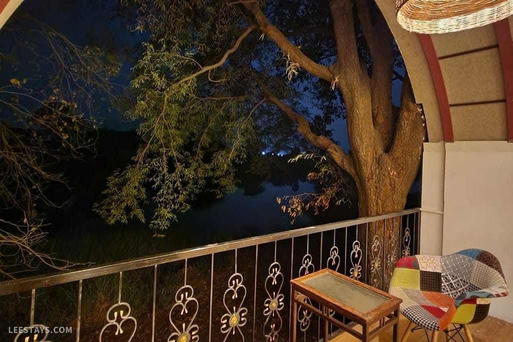 A peaceful evening view from a resort in Kamshet, featuring a balcony with a colorful chair and a large tree nearby.