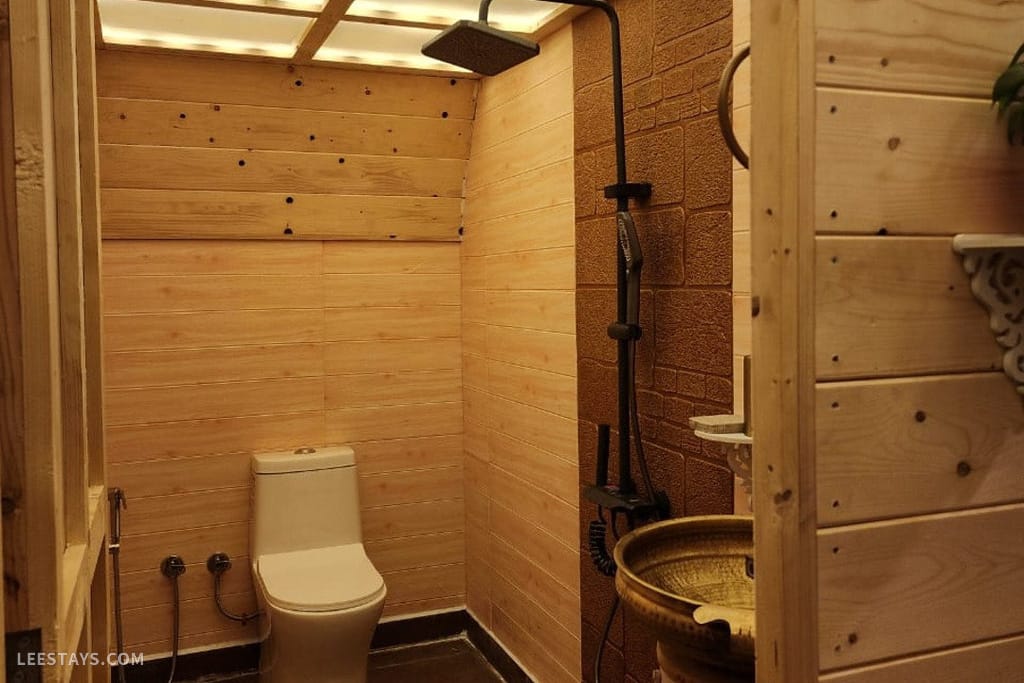 Modern bathroom with wooden paneling, featuring a toilet, shower, and decorative washbasin, set in a resort in Kamshet.