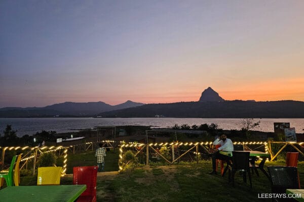 Evening scene at Pawna Lake featuring colorful seating, decorative lights, and mountains in the background under a twilight sky.