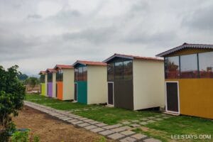 Colorful accommodations lined along a pathway, set against a cloudy sky near Pawna Lake, ideal for a relaxing stay.