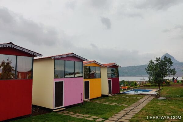 Colorful accommodation by Pawna Lake with a scenic backdrop, featuring a garden and pool area for a relaxing stay.