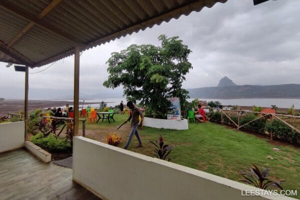 A scenic view of Pawna Lake with colorful seating areas, lush greenery, and people enjoying the serene atmosphere on a cloudy day.