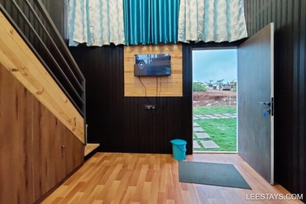 Contemporary interior with wooden accents, featuring a staircase, TV, and an outdoor view of Pawna Lake through an open door.