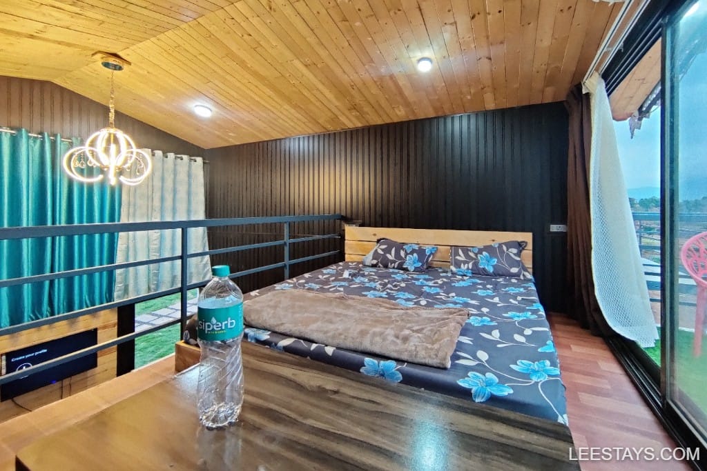 Cozy interior view of a stylish stay at Pawna Lake, featuring a floral bedspread and modern decor with large windows.