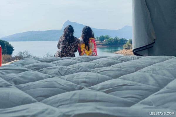 Two friends enjoying a glamping experience at Pawna Lake, with breathtaking views of the serene water and mountains in the background.