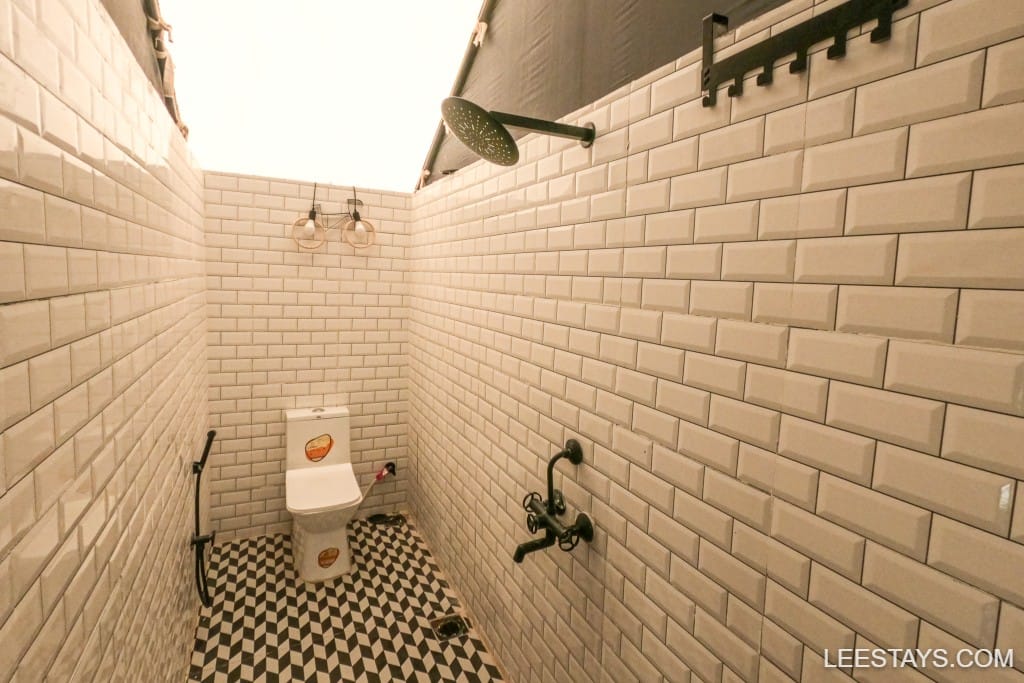 Stylish outdoor restroom with modern fixtures, ideal for glamping at Pawna Lake, featuring white tiles and checkered flooring.