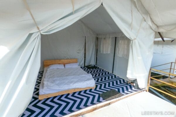 Stylish glamping setup near Pawna Lake, featuring a cozy bed on a chevron-patterned floor with ample natural light.