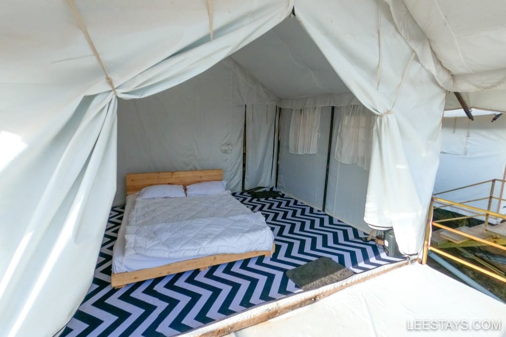 Stylish glamping setup near Pawna Lake, featuring a cozy bed on a chevron-patterned floor with ample natural light.