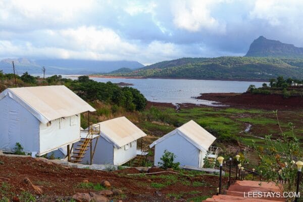 Glamping setup near Pawna Lake, featuring stylish white accommodations with scenic views and lush greenery around.