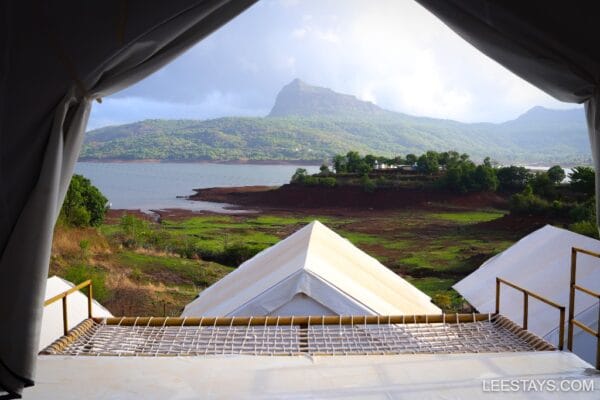 View from a glamping site at Pawna Lake, showcasing serene waters, lush greenery, and distant mountains under a cloudy sky.
