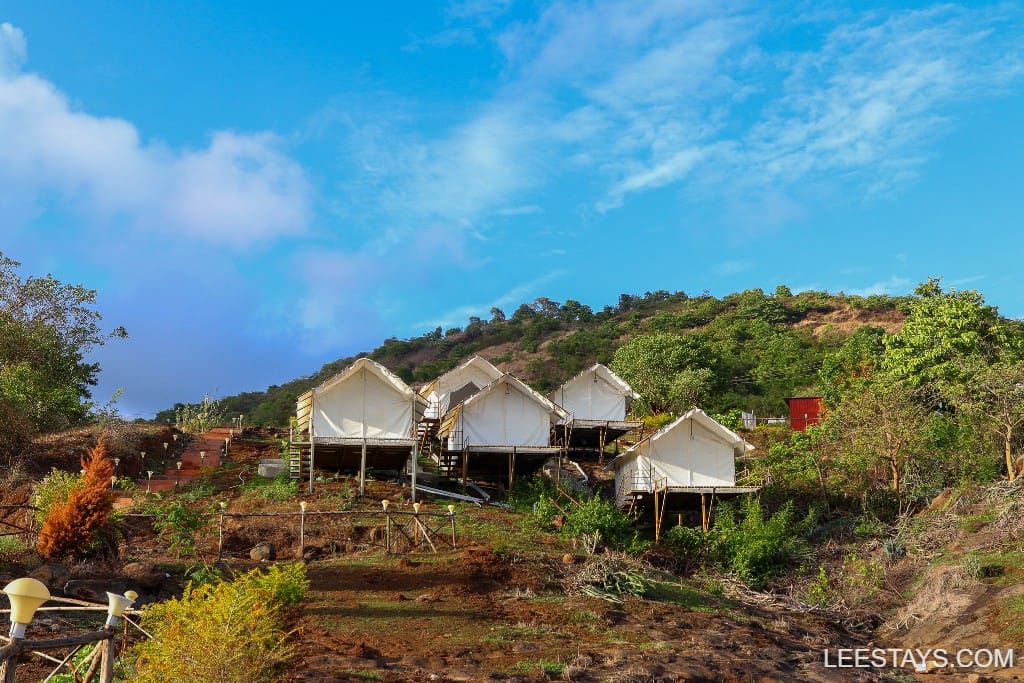 Glamping accommodations overlooking Pawna Lake, nestled on a hillside with lush greenery and blue sky.
