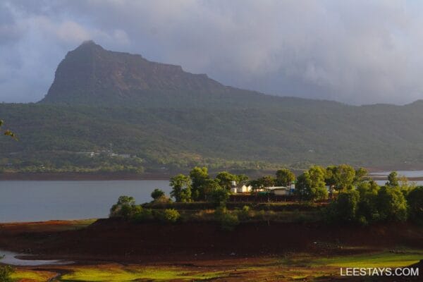 Scenic view of Pawna Lake surrounded by lush mountains, showcasing a serene glamping site near the water, with vibrant greenery.