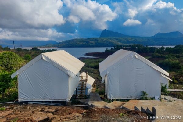 Glamping accommodations near Pawna Lake, surrounded by lush greenery and picturesque hills under a cloudy sky.