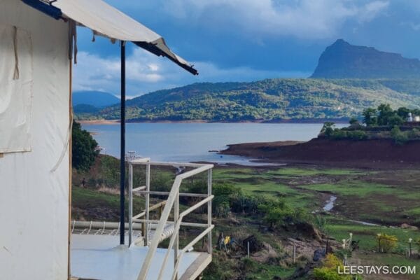 Serene glamping experience by Pawna Lake, offering stunning views of mountains and calm waters under a cloudy sky.