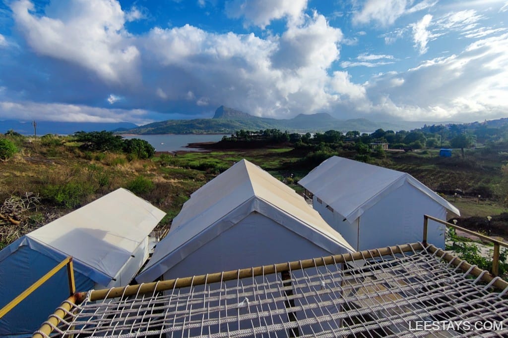 A scenic glamping site near Pawna Lake with white structures against a backdrop of hills and a vibrant sky.