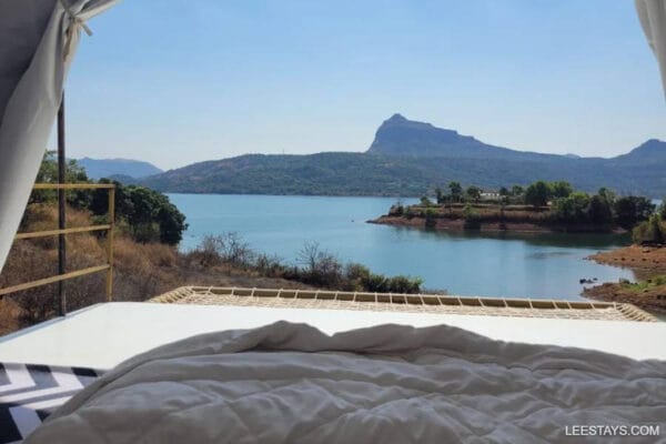 A serene glamping setup overlooking the calm waters of Pawna Lake, framed by distant mountains and greenery.