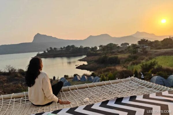 A person enjoying glamping at Pawna Lake, with a scenic view of hills and water at sunset.