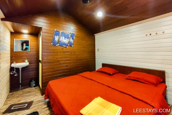 Cozy room with red bedding in a wooden cottage, perfect for family stays near Pawna Lake, featuring a sink and decorative art.