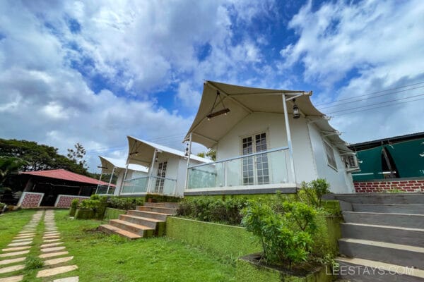 Charming cottages near the Pawna River, featuring contemporary architecture and a lush green landscape under a scenic sky.
