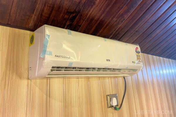 An indoor air conditioner unit on a wooden wall, ideal for cooling cottages at Pawna lake, providing comfort for couples seeking a relaxing getaway.