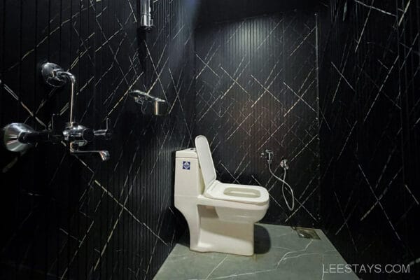 A modern bathroom with black wall tiles and a white toilet, suitable for a couple's stay in cottages near Pawna Lake.