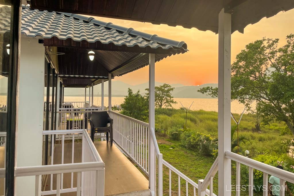 Cottages overlooking the serene Pawna Lake, perfect for a romantic couple's getaway, with a beautiful sunset and lush greenery in the background.