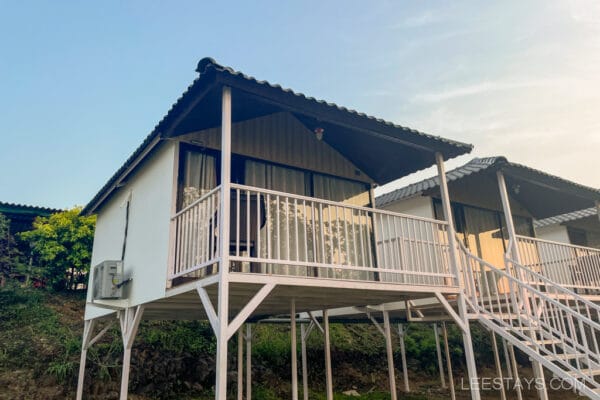 Scenic view of white cottages on stilts near Pawna Lake, ideal for a couple's getaway, surrounded by nature and evening sky reflections.