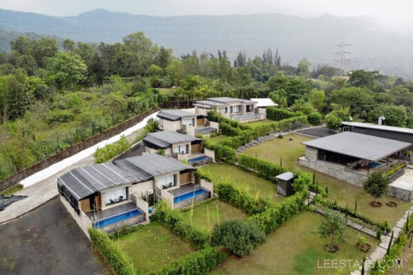 Aerial view of a resort by Pawna Lake with villas surrounded by lush greenery and a mountain backdrop.
