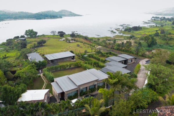 Aerial view of a resort near Pawna Lake, featuring lush greenery, modern buildings, and a scenic lakeside setting with distant hills.