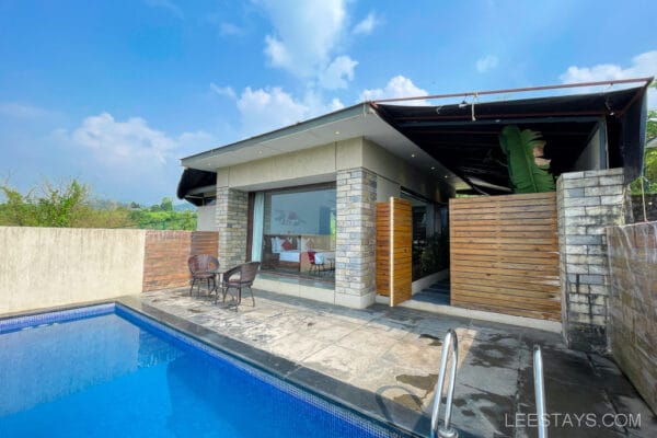 A modern resort villa at Pawna Lake with a private swimming pool, outdoor seating, and a scenic view under a clear blue sky.