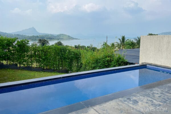 Resort near Pawna Lake featuring an infinity pool overlooking lush greenery and the serene water, set against a backdrop of distant mountains.