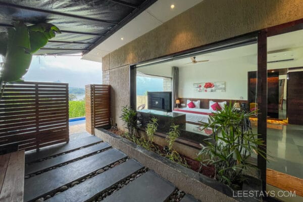 A luxurious resort room at Pawna Lake with large glass windows, modern furnishings, and a scenic view of the lake and surrounding greenery.