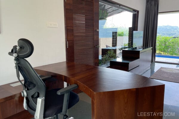 Modern office setup in a resort near Pawna Lake, featuring a wooden desk, ergonomic chair, and a view overlooking greenery and a pool.
