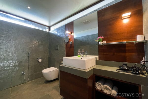 Modern bathroom at a resort near Pawna Lake, featuring a sleek sink, mirror, towels, and amenities on a polished counter, with a stone-tiled wall and floor.
