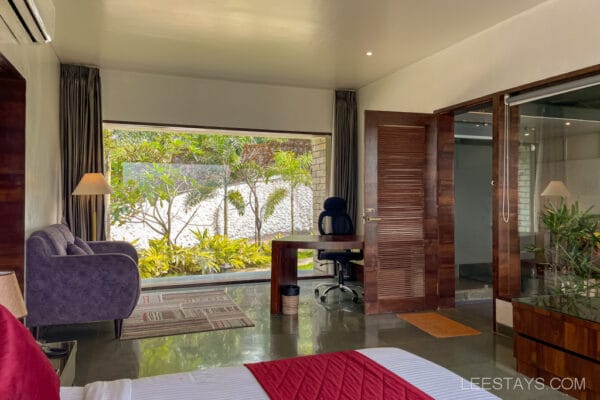 Modern resort room near Pawna Lake with large window view of lush greenery, featuring a desk, chair, and cozy seating area for relaxation.