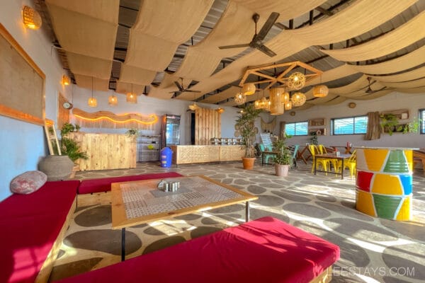 Interior of a cozy glass room near Pawna Lake with red cushioned seating, colorful decor, and large windows providing natural light.